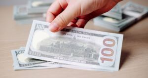 Hand adding dollar to large stack.