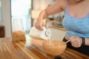 Woman pouring milk into a bowl with corn flakes for healthy nutrition. Breakfast, food and lifestyle concept