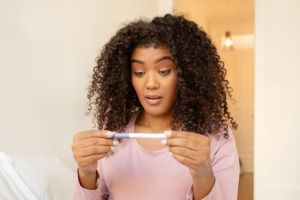 Shocked black woman checking pregnancy test at home, feeling surprised with result