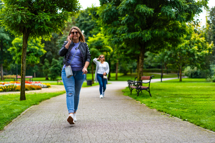 Two mature women walking separately in public park.