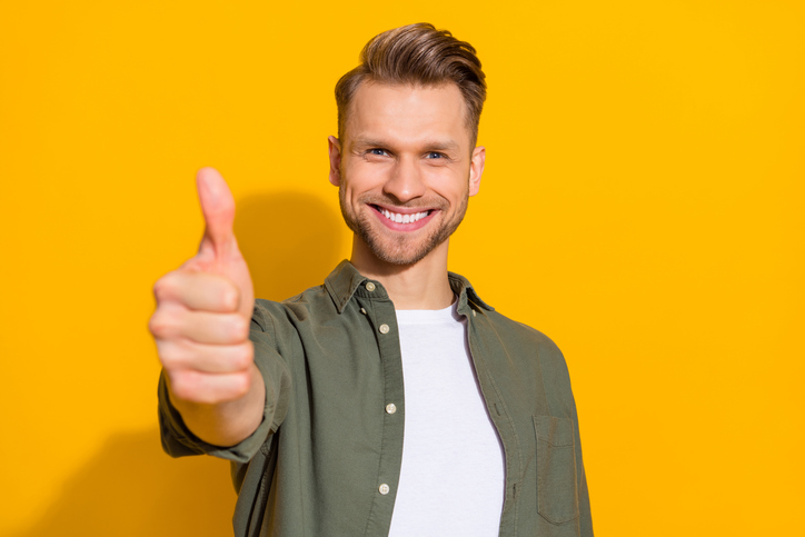 Portrait of attractive cheerful content guy giving thmbup ad advert isolated over bright yellow color background