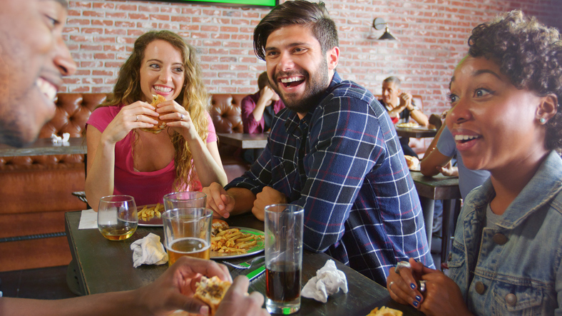 Group Of Friends Sitting Around Table Eating Out In Sports Bar