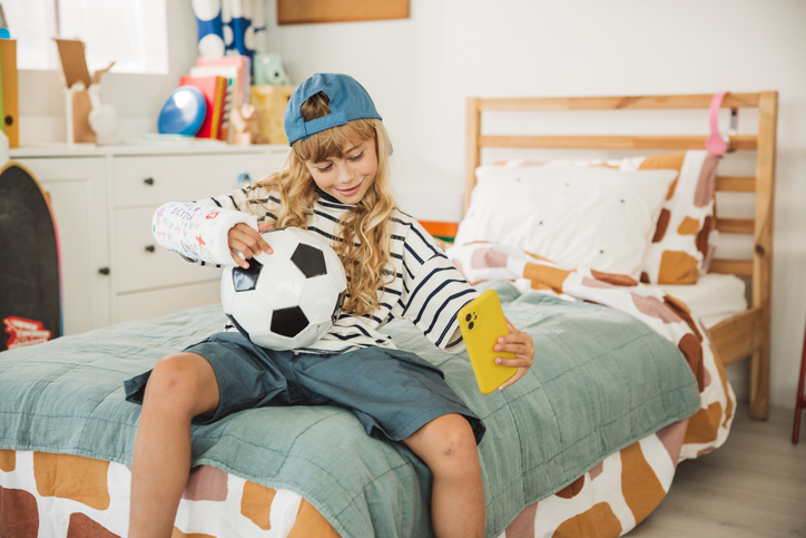 Cute girl with soccer ball and broken arm in orthopedic cast