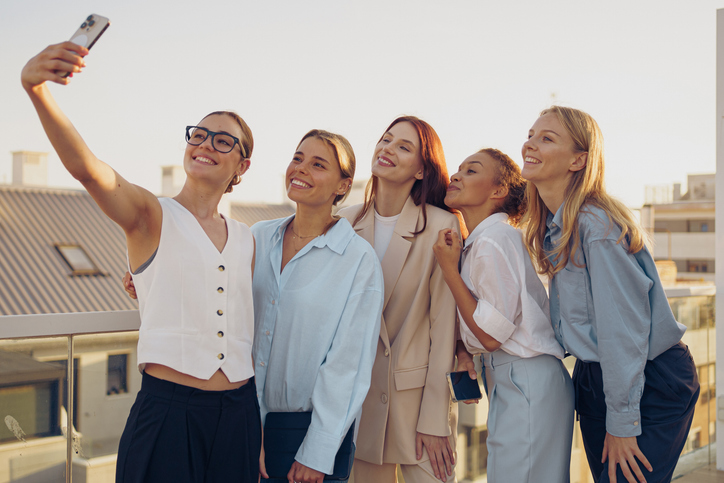 A group of friends happily taking a joyful selfie together on a rooftop during sunset time