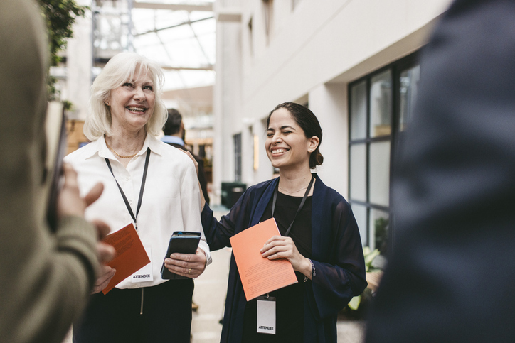 Happy businesswoman with hand on shoulder of female colleague standing in convention center